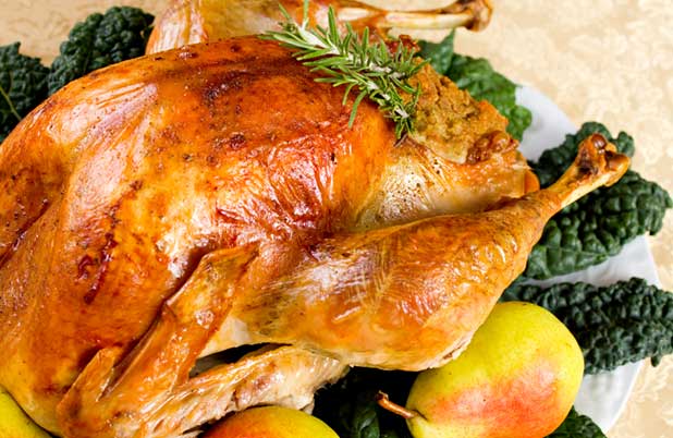 A whole turkey on a platter with fresh greens, a whole pear and rosemary sprigs.