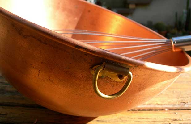 A whisk rests on the side of a copper bowl.
