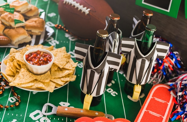 A Game Day spread with sliders, beer in referee bottle coolers and chips and salsa on a table with a football.