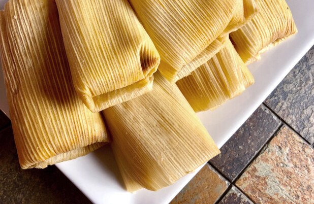 A stack of tamales wrapped in corn husk on a white plate.