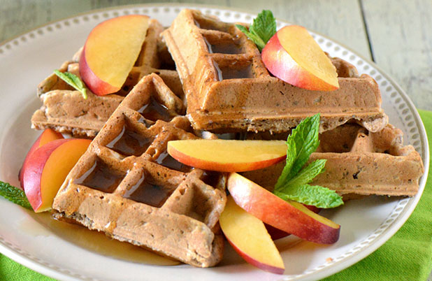 A plate filled with waffles, syrup and apple slices garnished with mint.