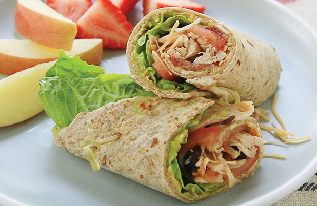 Sliced apples and strawberries beside a shredded chicken wrap on a blue plate.