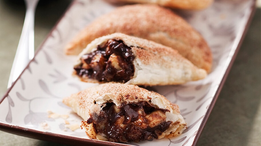Fresh baked chocolate and banana empanada cut in half showing the inside on a ceramic serving tray.