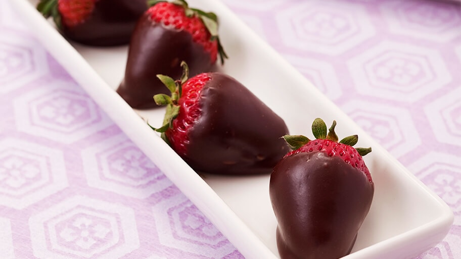 Chocolate covered strawberries in a long, thin ceramic serving tray on purple modern tablecloth.