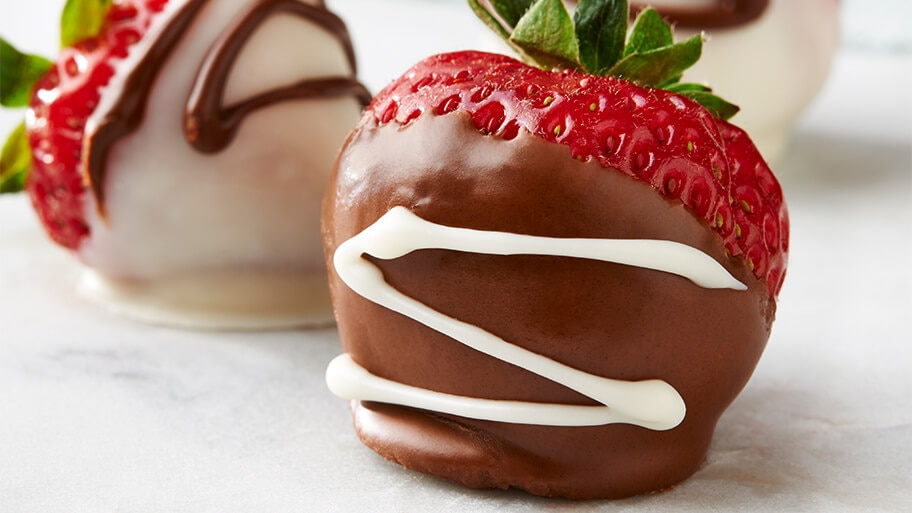Close up of milk chocolate covered strawberry with and a white chocolate covered strawberry on a marble table.