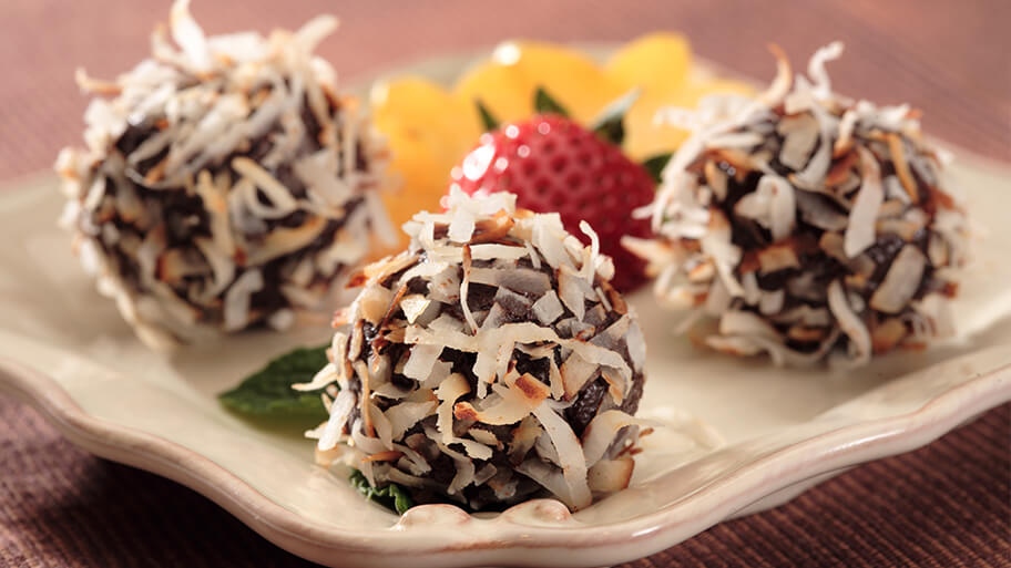 Coconut truffles with perfectly toasted fresh coconut stuck to chocolate on ceramic serving tray with fresh fruit.