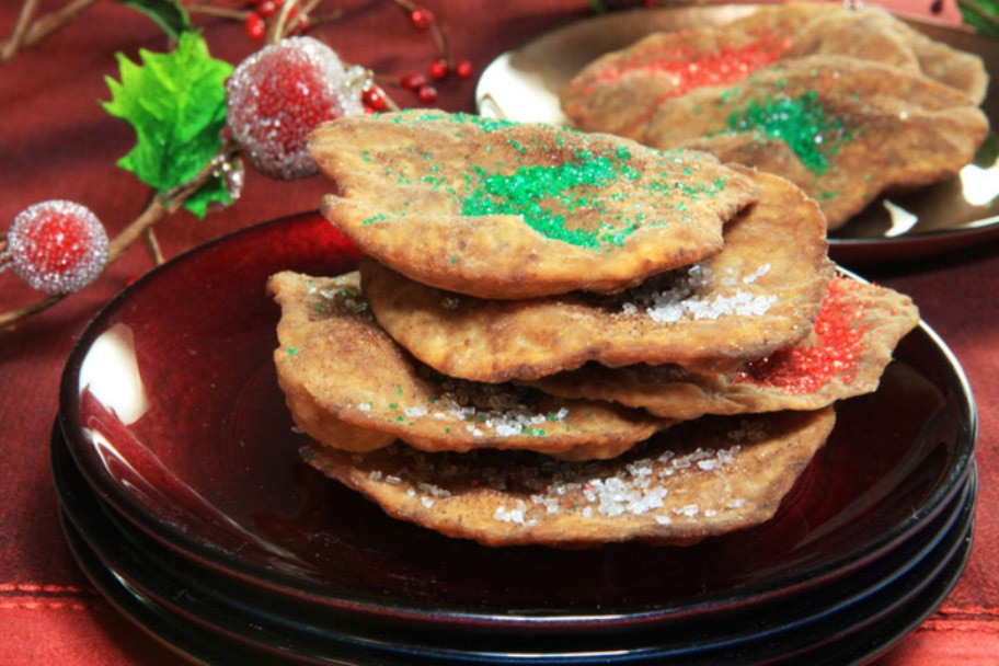 A stack of chocolate buñuelos on brown plates and a red tablecloth near holly branches.