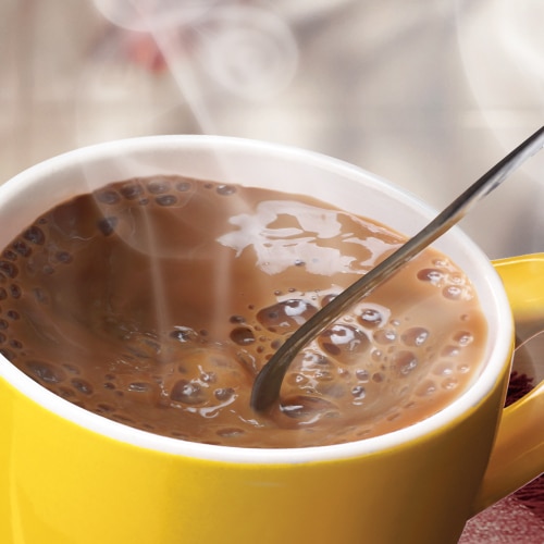 A spoon stirs a yellow mug full of hot chocolate.