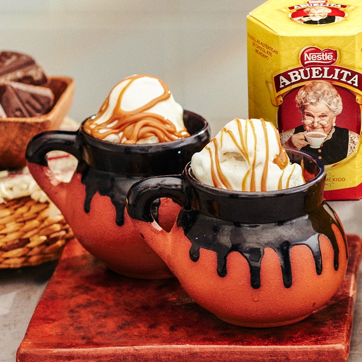 Dos tazas de cerámica rellenas de helado y caramelo cerca del empaque de tabletas ABUELITA.