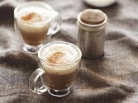 Dos tazas con espresso y creamer Coffee mate Café Mocha y crema batida con cacao por encima sobre un mantel de yute marrón.