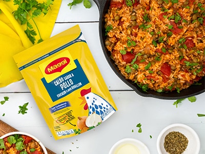 Granulated Chicken Flavor Bouillon Doypack near rice with pigeon peas and bowls of spices on a white table background.