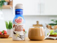 Botella de creamer vegetal Coffee mate French Vanilla Almond and Oat junto a una taza de vidrio llena de café y creamer.