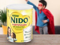 Envase de Nido Fortificada sobre una mesa con un niño disfrazado de superhéroe y una planta al fondo.