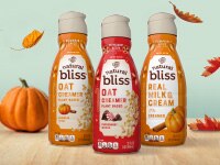 Pumpkin Spice Real Milk & Cream, Peppermint Mocha & Pumpkin Spice Oat Creamers next to pumpkins & leaves on a wood surface.