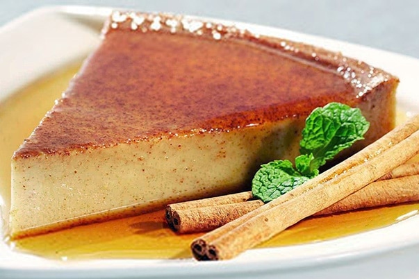 A slice of flan with cinnamon sticks and fresh mint.