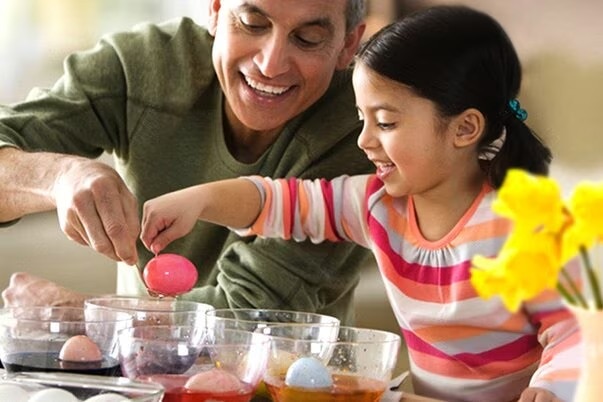 A dad helps his daughter dye an Easter egg pink.