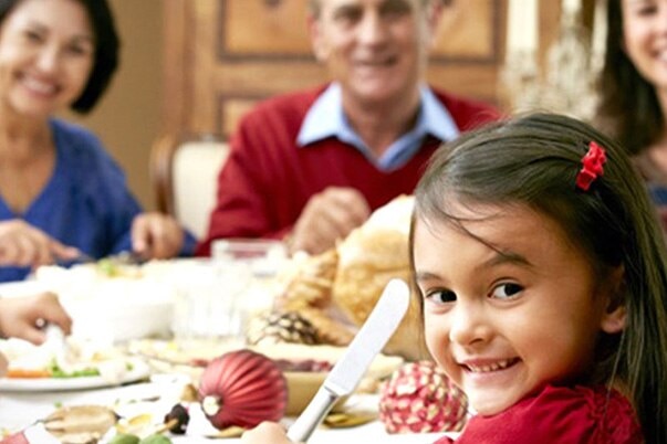 A family smiles for a photo as they gather around a festive table for Christmas dinner.