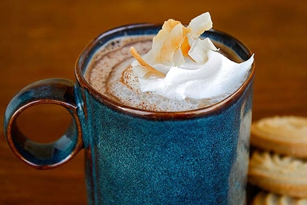 A blue mug filled with Abuelita™ Mexican hot chocolate and whipped cream along with some cookies.