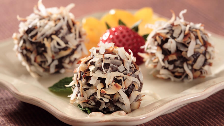 Coconut truffles with perfectly toasted fresh coconut stuck to chocolate on ceramic serving tray with fresh fruit.