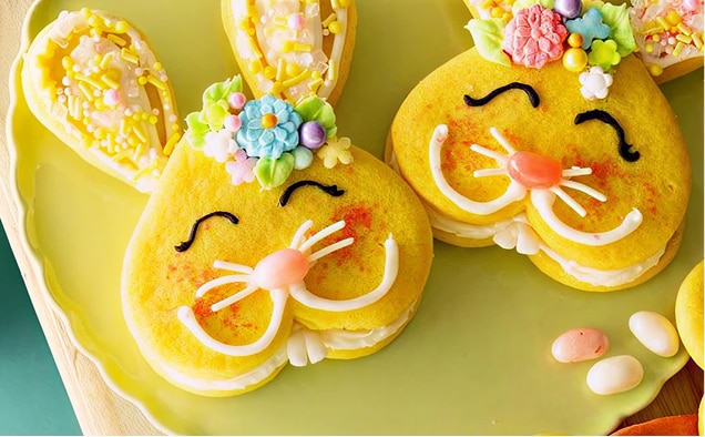 Photograph of three smiling yellow bunny macarons with floral icing on a green plate