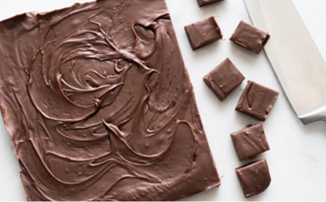 Photograph of glossy chocolate ganache spread on a rectangle, sliced into squares, knife beside