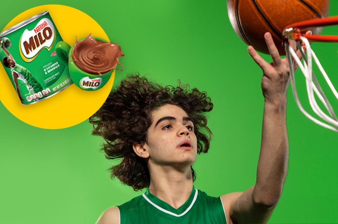 Un adolescente con uniforme verde empuja un balón de básquetbol hacia dentro de una canasta.
