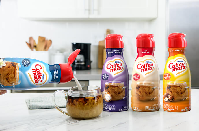 Bottles of Italian Sweet Creme, Original, Hazelnut next to French Vanilla creamer being poured into coffee on a countertop.