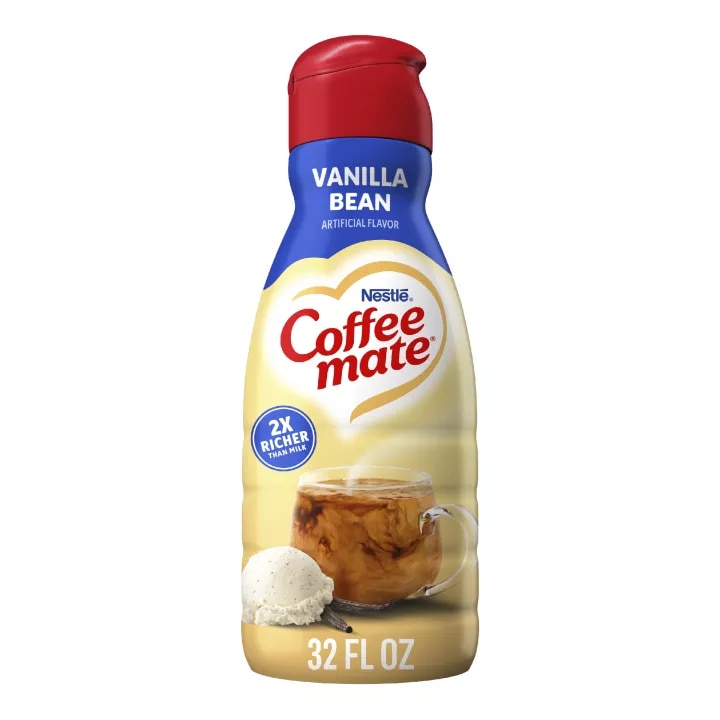 Una botella de creamer Vanilla Bean con una etiqueta azul sobre una taza azul y un tazón de helado de vainilla junto a una vaina de vainilla.