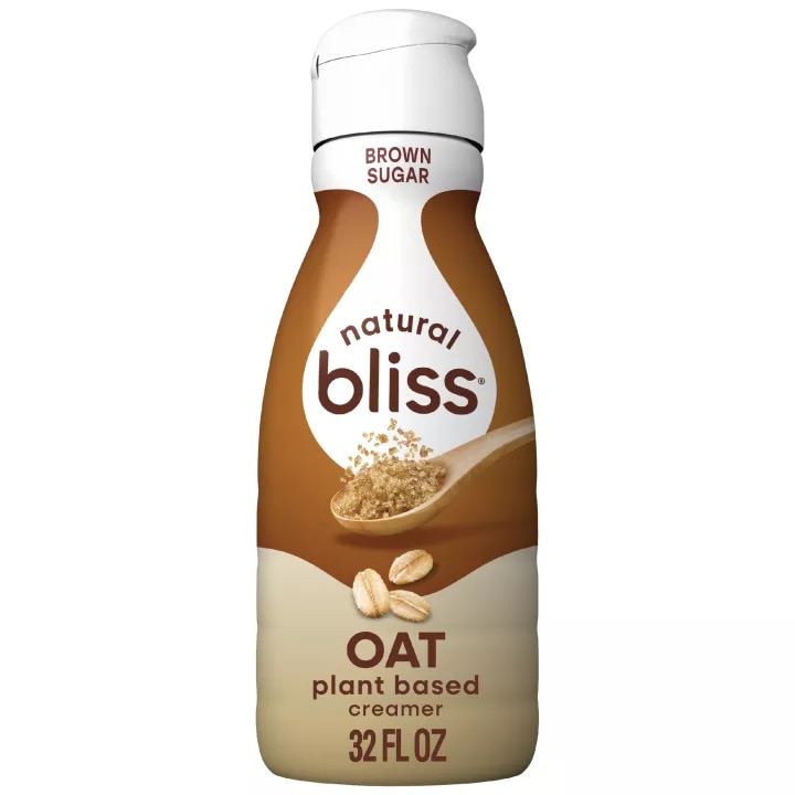 Una botella de creamer Oat Brown Sugar de natural bliss con una etiqueta marrón encima de una taza medidora con azúcar moreno.