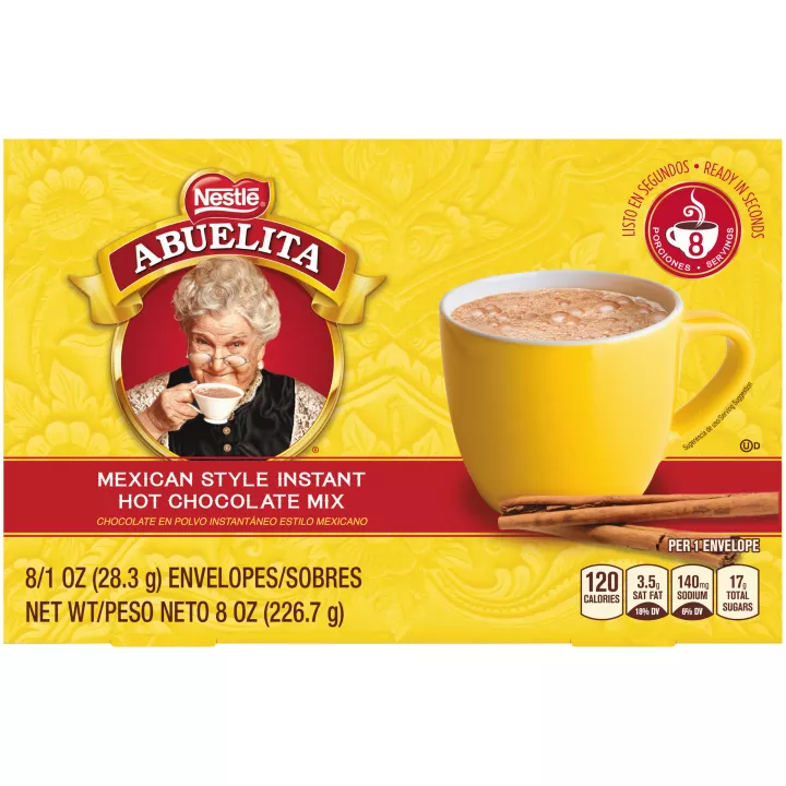 A yellow box with a red label below a yellow mug of Mexican hot chocolate behind cinnamon sticks.