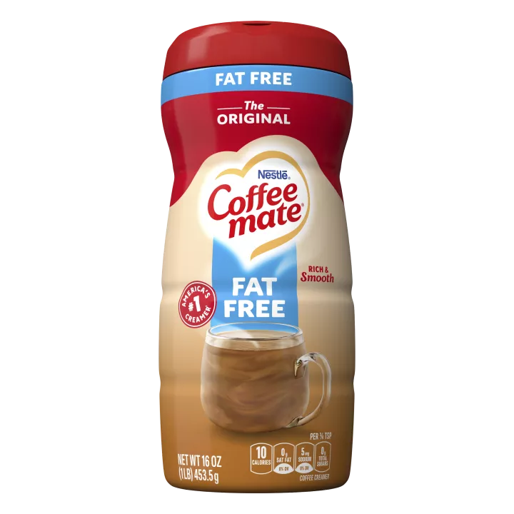 Una lata de creamer en polvo Coffee mate Original sin grasa con una tapa roja y una etiqueta azul encima de una taza de café con un biscotti.