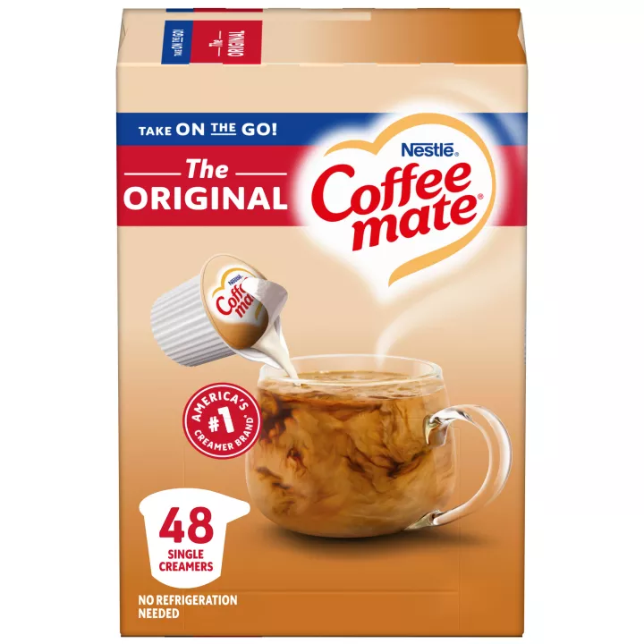 Una caja de porciones individuales de creamer original Coffee mate con una etiqueta roja, una taza de café, un biscotti y el logotipo de Coffee mate.
