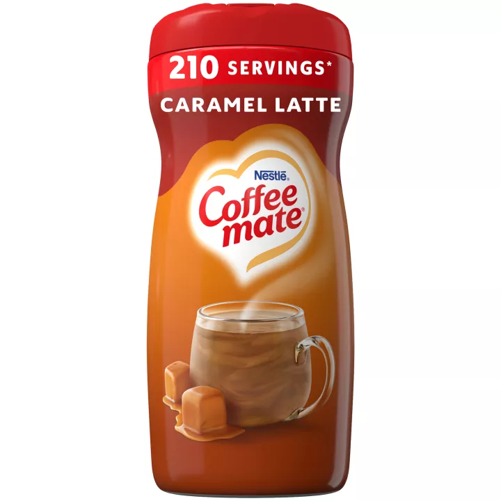 Una lata marrón de creamer Coffee mate Caramel Latte con una etiqueta roja encima de una taza de café con gotas de caramelo.