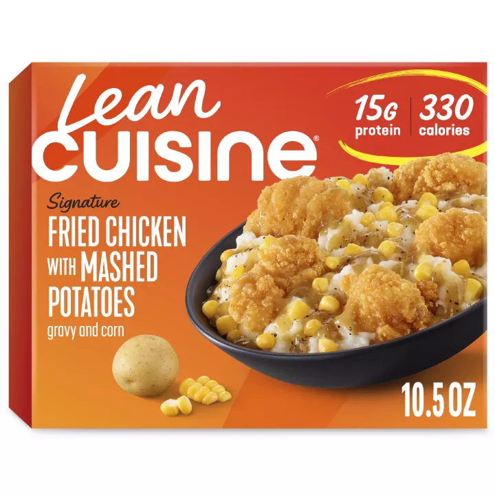 A box of oven fried chicken with mashed potatoes with Protein Kick label with 300 calories, 14 grams of protein and half cup of veggies near a bowl of corn, chicken and potatoes.