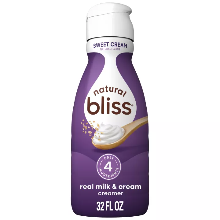 White bottle of natural bliss Sweet Cream flavored Creamer with a purple label above a spoon of sugar and swirl of milk.