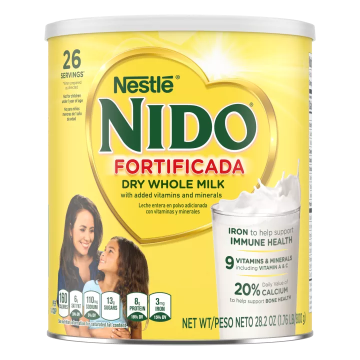 A canister of Nido Fortificada with a yellow label, white lid and gold heart above a glass of milk pouring.
