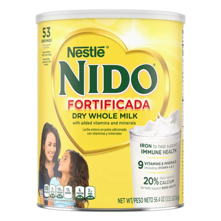 Una lata de Nido Fortificada con una etiqueta amarilla, una tapa blanca y un corazón dorado sobre un vaso de leche vertida.