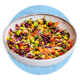 Primer plano de un tazón blanco con una ensalada vegetariana sobre un fondo azul.