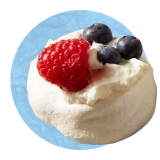 Primer plano de un mousse de vainilla con frambuesas y arándanos por encima sobre un fondo azul.