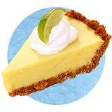Primer plano de un trozo de key lime pie con una cucharada de crema batida por encima y un gajo de lima sobre un fondo azul.