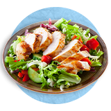  Primer plano de un tazón de madera con hojas verdes y una pechuda de pollo en rodajas por encima sobre un fondo azul.