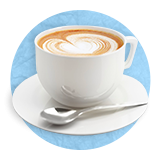 Close up of a white mug of cappuccino on a white saucer with a small spoon for stirring on it, on a blue background. 