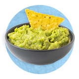 Primer plano de un tazón azul con guacamole con un chip de tortilla como decoración sobre un fondo azul.
