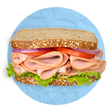 Close up of a turkey sandwich on whole wheat bread with lettuce and tomato on a blue background.