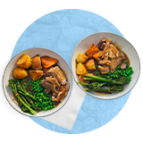 Plano aéreo de dos platos blancos con bistec, papas asadas y espinacas sobre un fondo azul.