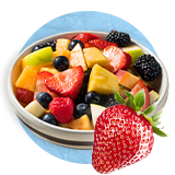 Primer plano de un tazón blanco con ensalada de fruta y una fresa entera sobre un fondo azul.