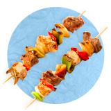 Primer plano de un par de brochetas de pollo y vegetales sobre un fondo azul.