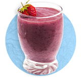 Close up of a clear glass with purple smoothie filled to the top with a strawberry garnish, on a blue background.