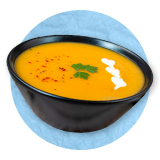 close up of a butternut squash soup in a black bowl, on a blue background.