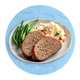 Primer plano de un plato blanco con un pastel de carne, puré y habichuelas verdes sobre un fondo azul.